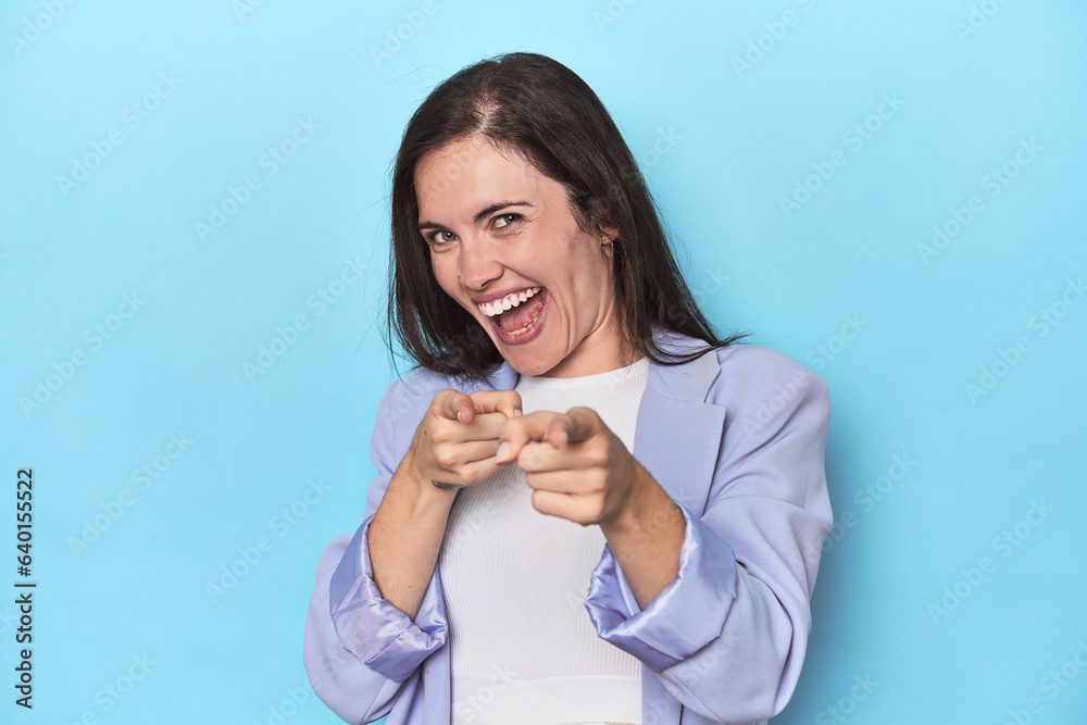 Woman in blue blazer on blue background pointing to front with fingers. Woman in blue blazer on blue background pointing to front with fingers.