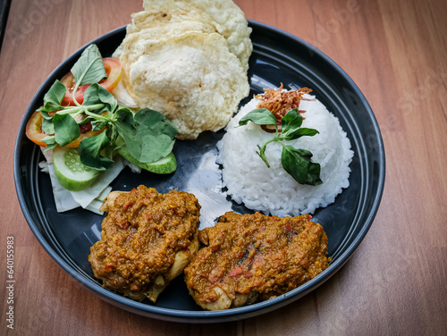 Ayam bakar Taliwang is a traditional roast chicken from Lombok Indonesia, isolated on a wooden background, served with vegetables. Spicy but tasty cuisine photo