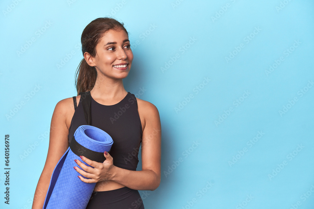 Young sportswoman holding a yoga mat in studio. Young sportswoman holding a yoga mat in studio.