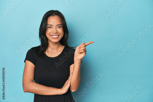 Filipina young woman on blue studio smiling cheerfully pointing with forefinger away.