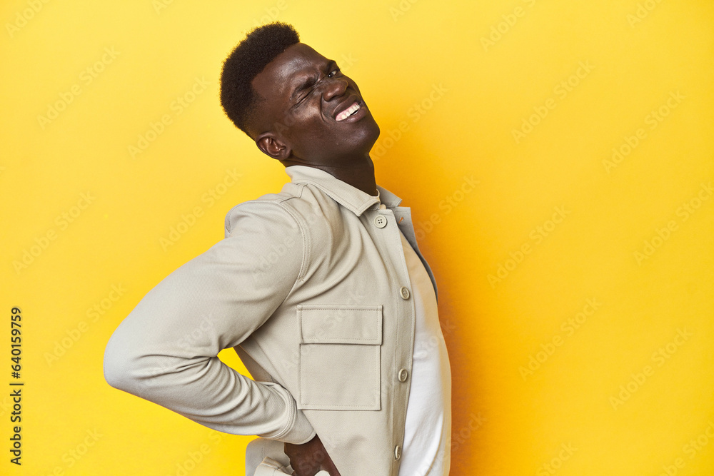 Stylish young African man on vibrant yellow studio background, suffering a back pain.