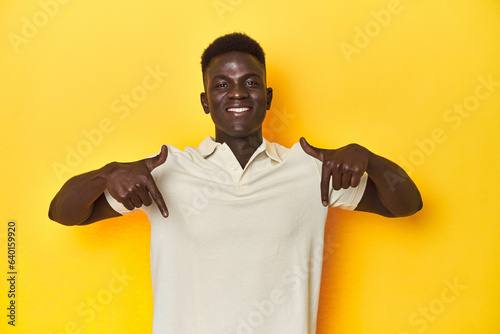 Stylish young African man on vibrant yellow studio background, points down with fingers, positive feeling.
