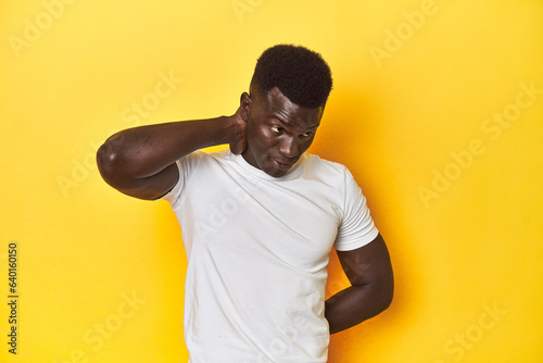 Stylish young African man on vibrant yellow studio background, suffering neck pain due to sedentary lifestyle.