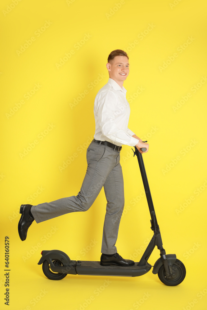 Happy man riding modern electric kick scooter on yellow background Happy man riding modern electric kick scooter on yellow background