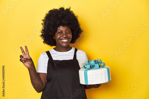 Baking woman with cake, a sweet treat prepared joyful and carefree showing a peace symbol with fingers.