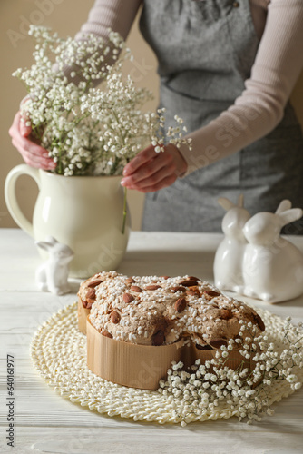 Delicious Italian Easter dove cake (traditional Colomba di Pasqua). Woman putting bouquet on white wooden table