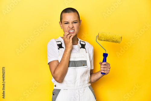 Painter woman, shaved head, with yellow roller in studio biting fingernails, nervous and very anxious.