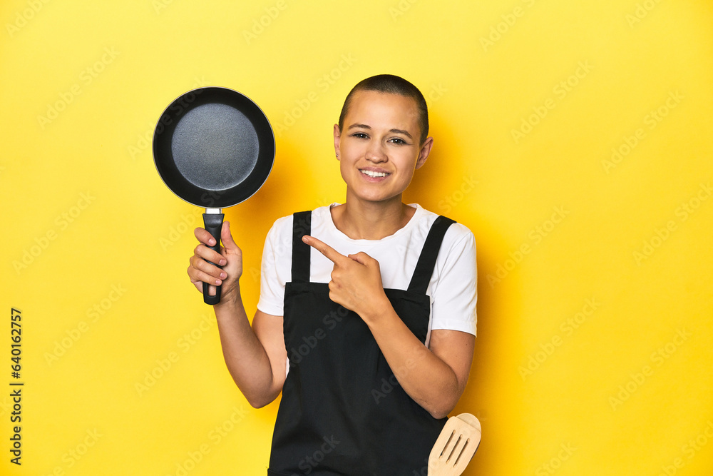 Cook woman holding a pan, yellow studio background smiling and pointing aside, showing something at blank space. Cook woman holding a pan, yellow studio background smiling and pointing aside, showing something at blank space.