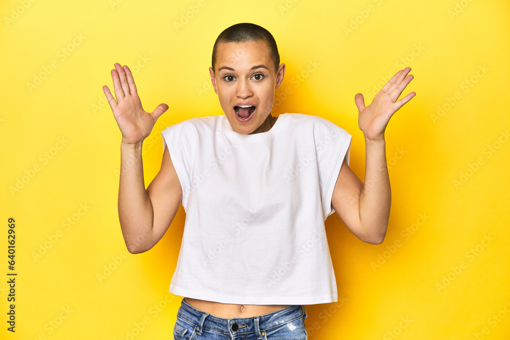 Shaved head woman in white tank top, yellow backdrop celebrating a victory or success, he is surprised and shocked. Shaved head woman in white tank top, yellow backdrop celebrating a victory or success, he is surprised and shocked.
