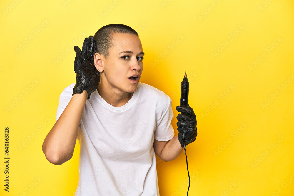 Tattooist woman in studio, shaved head, yellow background trying to listening a gossip. Tattooist woman in studio, shaved head, yellow background trying to listening a gossip.