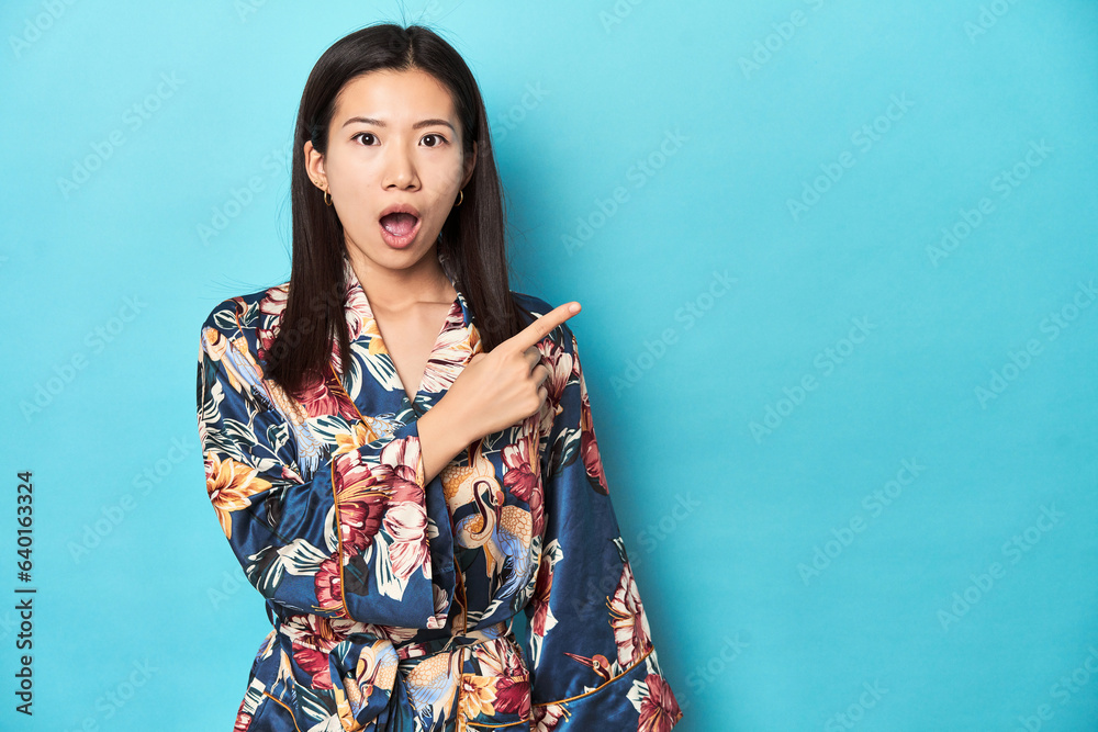 Elegant young Asian woman in kimono, studio shot pointing to the side Elegant young Asian woman in kimono, studio shot pointing to the side