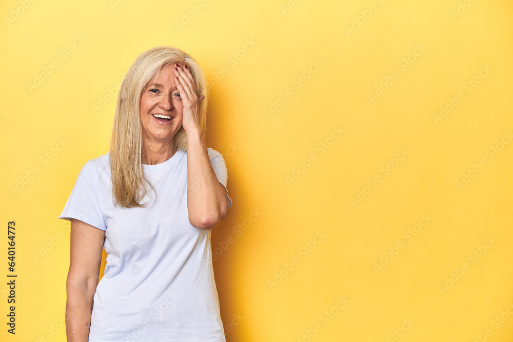 Middle-aged Caucasian woman in white t-shirt, yellow studio laughing happy, carefree, natural emotion. Middle-aged Caucasian woman in white t-shirt, yellow studio laughing happy, carefree, natural emotion.