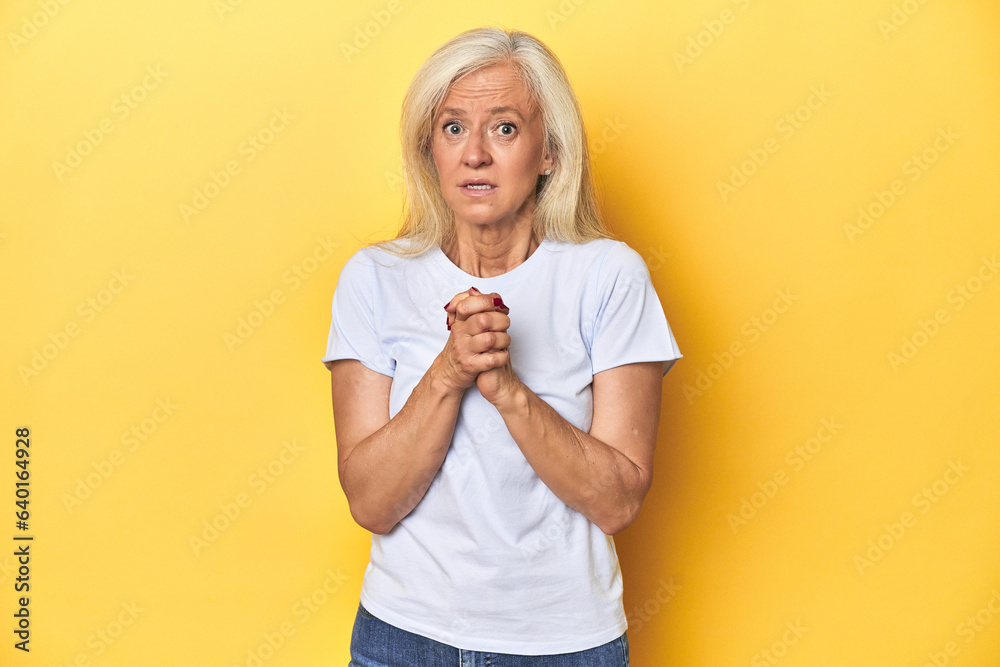 Middle-aged Caucasian woman in white t-shirt, yellow studio scared and afraid. Middle-aged Caucasian woman in white t-shirt, yellow studio scared and afraid.