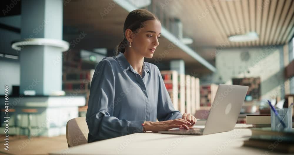 Beautiful Caucasian Female Student Working on Her School Thesis on a Laptop Computer. Young Smart Woman Sitting Behind a Desk, Studying an Online Course in an Empty Public Library with Modern Design