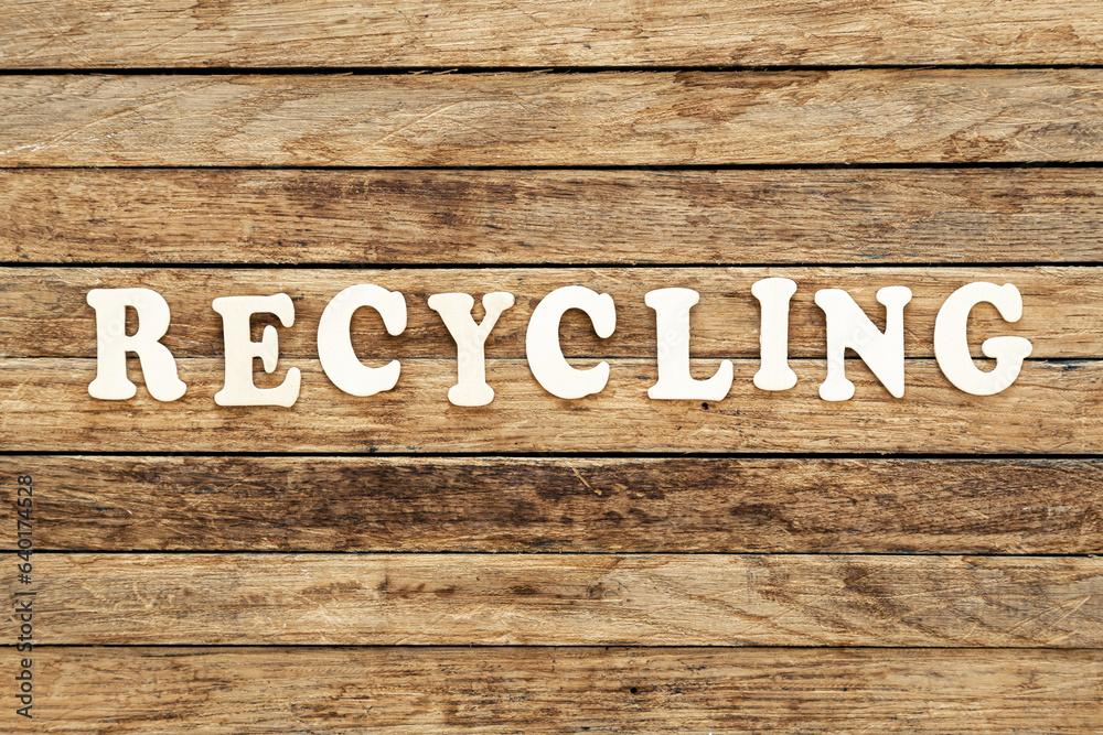 The word Recycling written on wood letters on wooden background, top view.