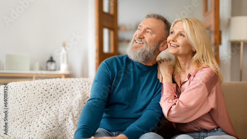 Romantic European Senior Spouses Looking Aside, Hugging Sitting At Home