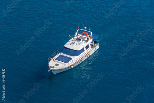 Yacht with sun loungers at the stern floating on the water surface in summer, aerial top view