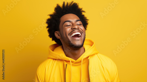 Young man laughs against a yellow background.