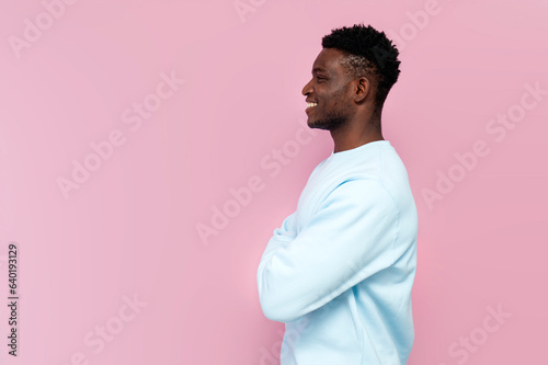 Konstfotografi african man in blue sweater smiles and stands with his arms crossed on pink isol