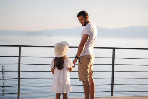 Back view of daughter with her father stand on heigh balcony in front of sea sunset. Dad with his little girl looking on mountains photo