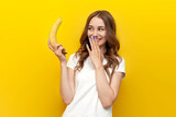 young girl holding small banana and mocking on yellow isolated background, woman presents erotic and intimate concept