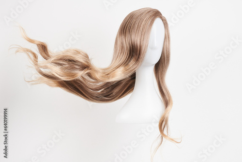 Natural looking blonde wig on white mannequin head. Long hair on the plastic wig holder isolated on white background. photo