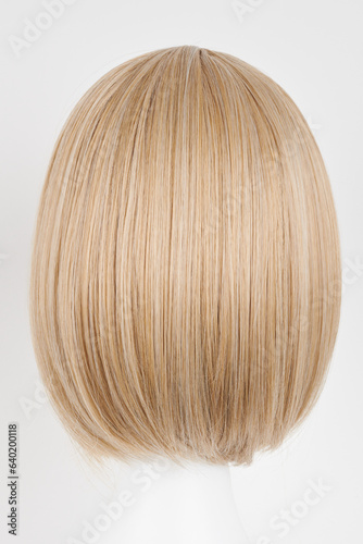 Natural looking blonde fair wig on white mannequin head. Short hair cut on the plastic wig holder isolated on white background, back view.