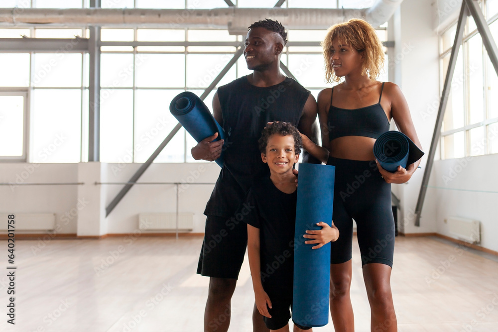 african american family in sportswear with yoga mat stands in the gym, mom dad and son on fitness workout