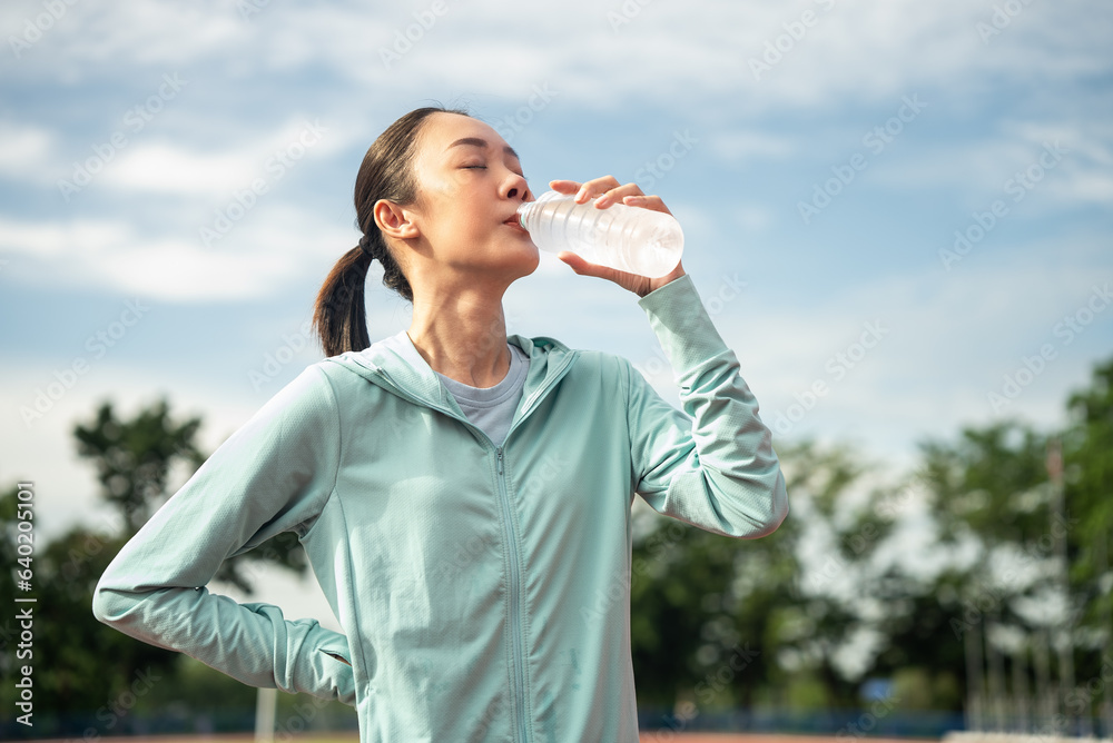 Close up beautiful asian woman drinking water from bottle after running with running track background, outdoor workout concept, drink clear mineral water after jogging. Generation z lifestyle. Close up beautiful asian woman drinking water from bottle after running with running track background, outdoor workout concept, drink clear mineral water after jogging. Generation z lifestyle.
