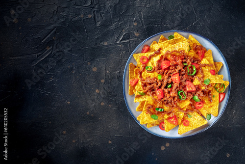 Nachos, Mexican food, tortilla chips with beef and fresh vegetables, shot from above on a dark stone background with copy space