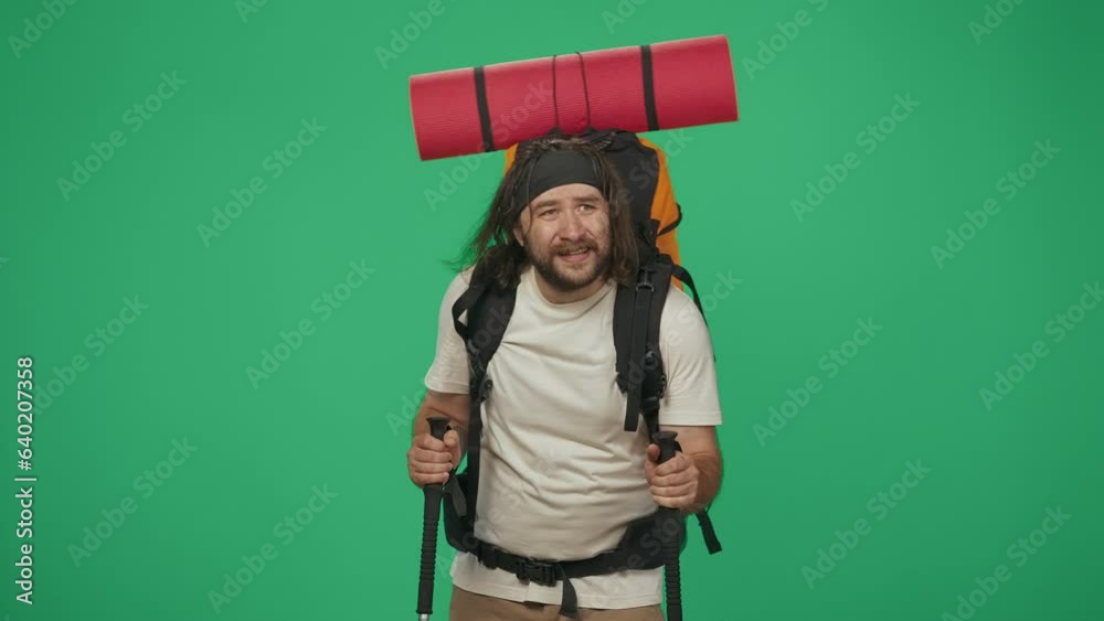 Man tourist with backpack walking with trekking poles, looks around, tired face expression. Isolated on green background. Man tourist with backpack walking with trekking poles, looks around, tired face expression. Isolated on green background.