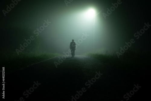 A dark silhouette on a foggy road at night
