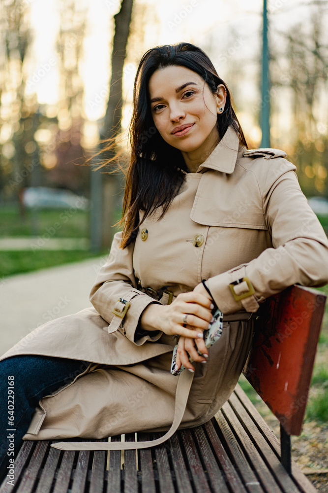 Beautiful young woman in coat relaxing on a bench in park Beautiful young woman in coat relaxing on a bench in park
