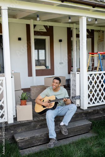 cheerful african american man playing acoustic guitar on porch near boxes and new house © LIGHTFIELD STUDIOS