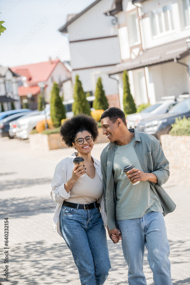 positive african american couple with takeaway coffee holding hands while walking on urban street positive african american couple with takeaway coffee holding hands while walking on urban street
