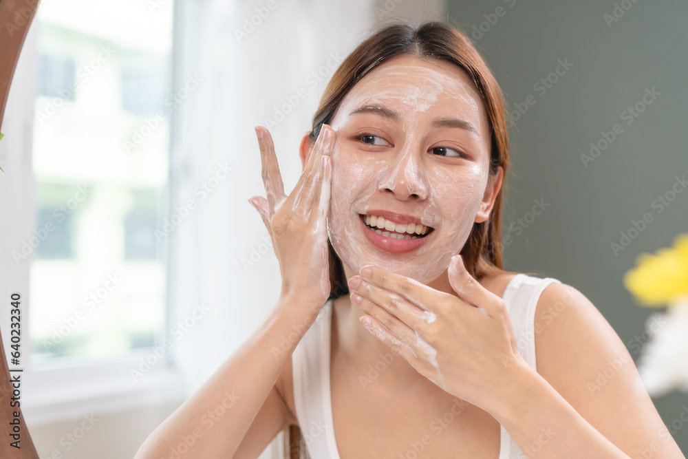 facial skin care routine concept. young woman looking in the mirror during washing her face with facial foam