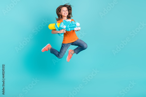 Photo of energetic cheerful girl wear stylish clothes have fun fly air hold water gun look empty space isolated on cyan color background