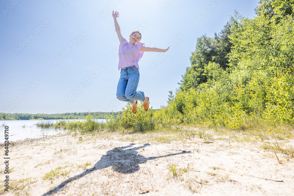 Capture the essence of boundless joy with this exhilarating image. An attractive young millennial Caucasian woman leaps into the air, arms spread wide in sheer happiness during her summer holiday at Capture the essence of boundless joy with this exhilarating image. An attractive young millennial Caucasian woman leaps into the air, arms spread wide in sheer happiness during her summer holiday at