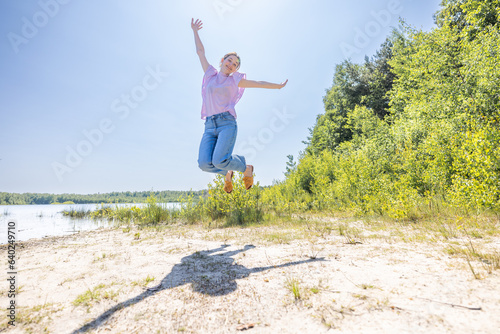 Capture the essence of boundless joy with this exhilarating image. An attractive young millennial Caucasian woman leaps into the air, arms spread wide in sheer happiness during her summer holiday at