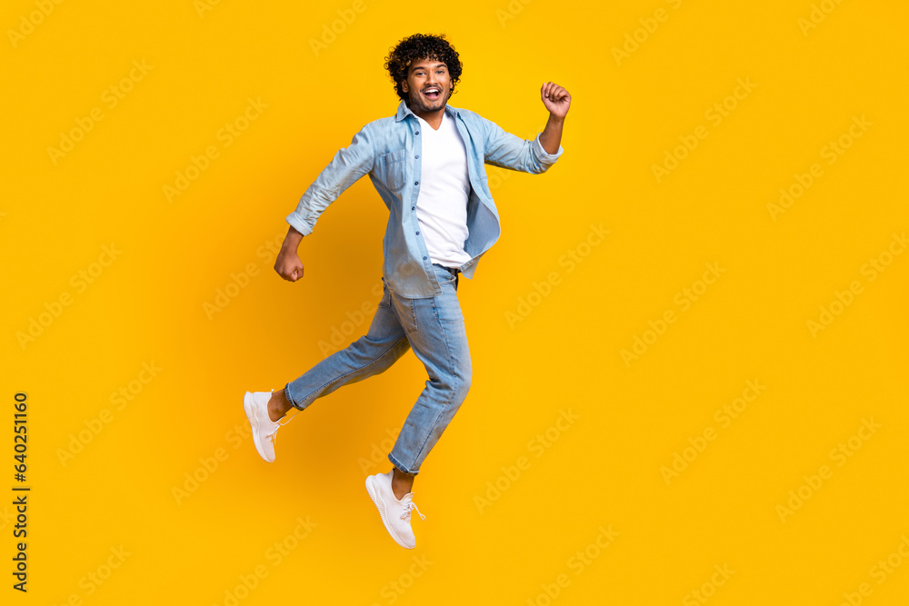 Full length photo of hurrying funny guy dressed denim jacket jumping high running fast empty space isolated yellow color background