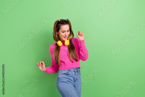 Photo of cheerful satisfied gorgeous woman dressed pink sweater in earphones dancing having fun isolated on green color background © deagreez