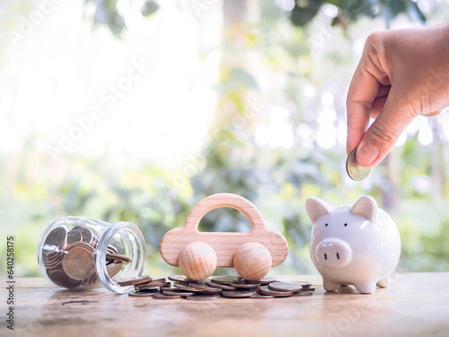 Close up of hand putting coins into piggy bank and wooden toy car on stack of coins. Transport and manage success business concept. Concept of car loan