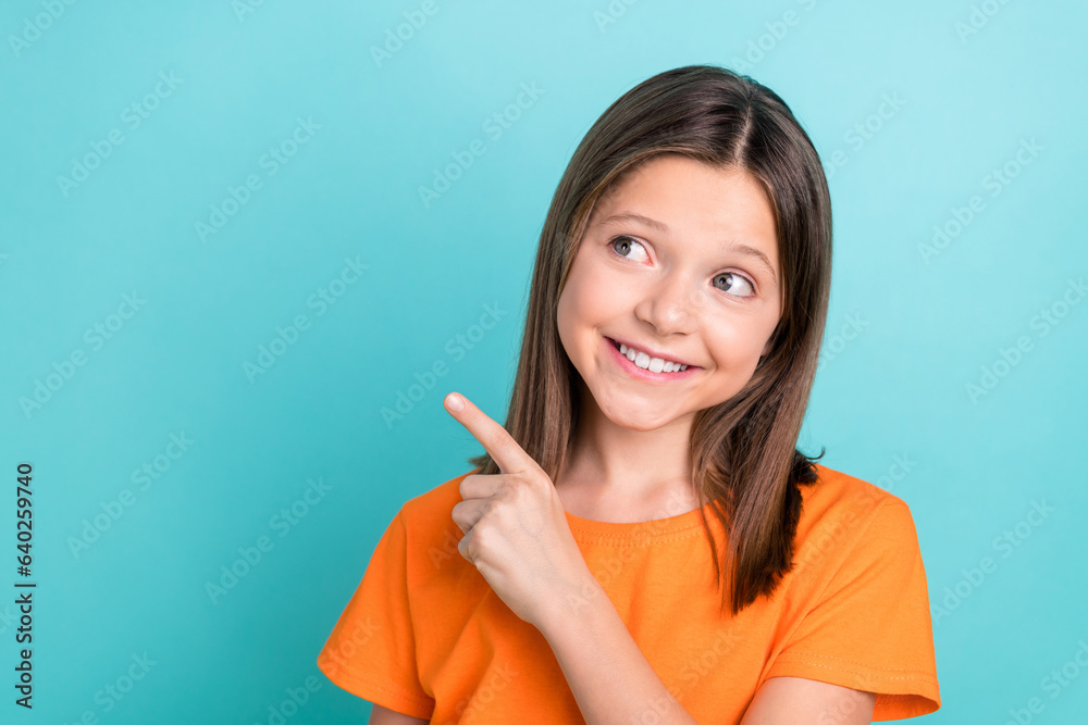 Photo of optimistic small girl wear stylish orange t-shirt look directing at discount empty space isolated on teal color background Photo of optimistic small girl wear stylish orange t-shirt look directing at discount empty space isolated on teal color background