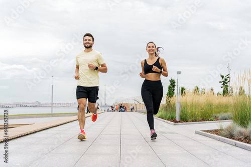 A personal trainer and a client teach fitness running. Male and female runners smile and train together. Instructors of friends use a fitness watch and a sports app. 
