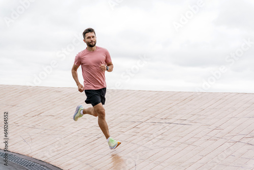 The running coach is a man and trains outdoors.  Runner athlete in fitness clothes and running shoes, full-length. Uses a fitness watch for a strong person and sports for health. © muse studio
