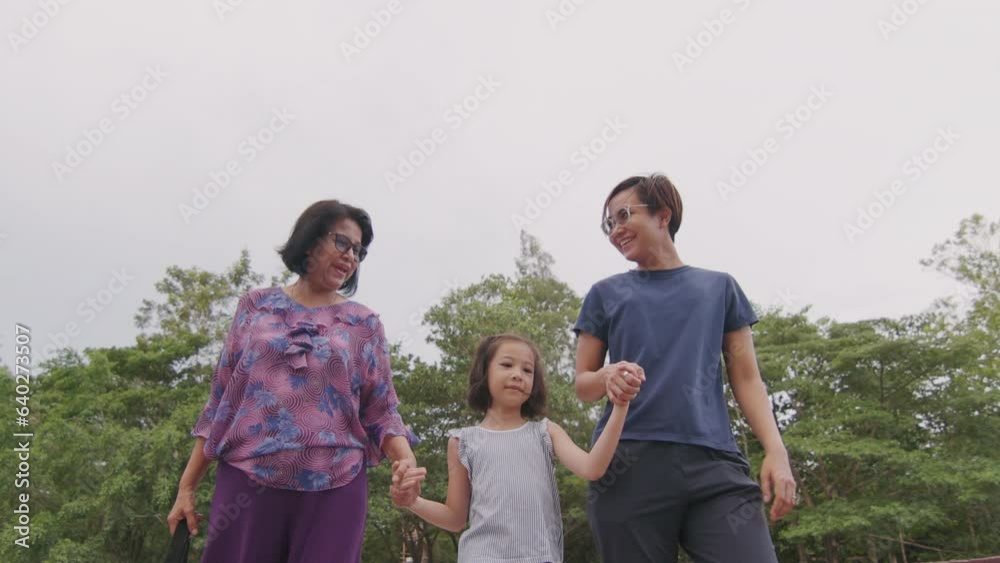 Beauty of diverse people sharing smiles and holding hands, walking in the greenery of a park. Asian senior woman is joyful with her daughter and granddaughter showing multi-generation family bonds. Beauty of diverse people sharing smiles and holding hands, walking in the greenery of a park. Asian senior woman is joyful with her daughter and granddaughter showing multi-generation family bonds.