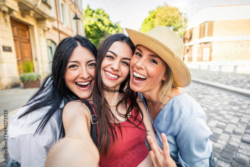 Happy female friends taking selfie with smart mobile phone device outside - Delightful young women having fun on summer vacation - Friendship concept with ladies enjoying day out