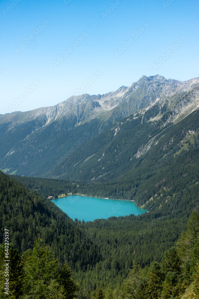 Aerial view of turquoise alpine mountain lake Lago di Anterselva (Antholzer See) as seen from Passo Stalle (Staller Pass) in a Dolomite mountain valley with green pine forest - obrazy, fototapety, plakaty 