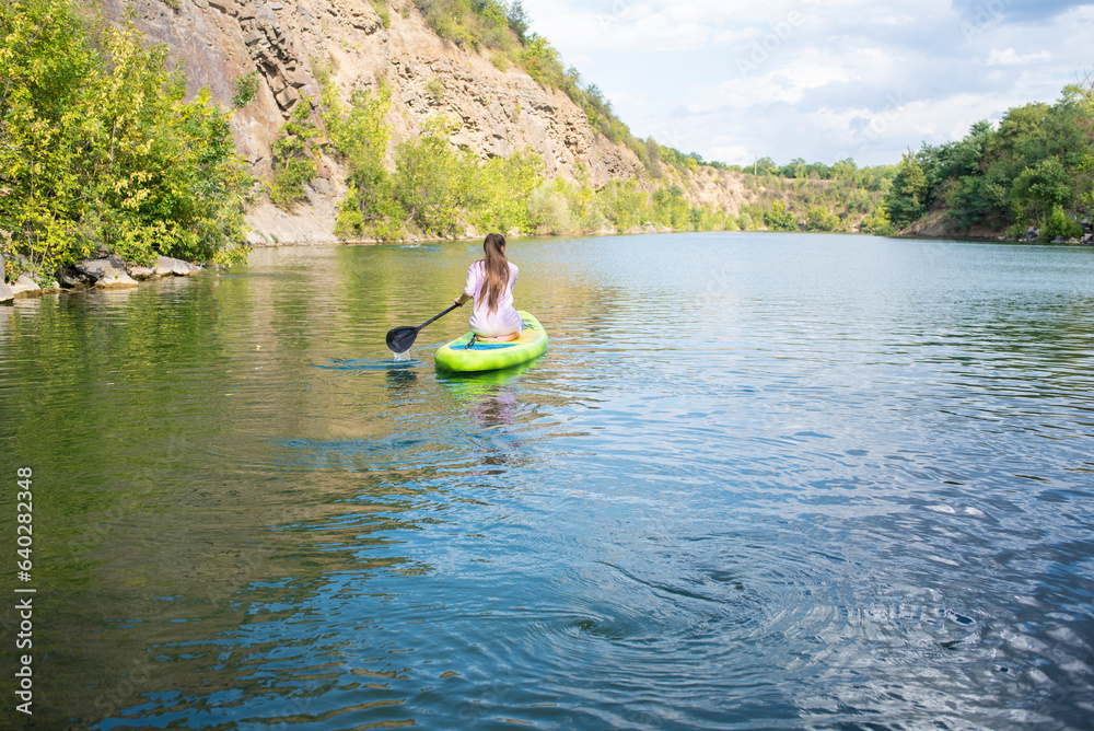 a teenage girl rides on a green SUP board on a beautiful mountain lake, Krasnosulinsky canyon in the Rostov region, in Russia.