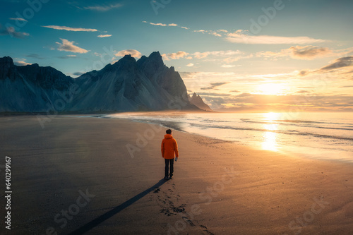 Vestrahorn mountain during sunrise and man standing on black sand beach in Stokksnes peninsula on summer at Iceland